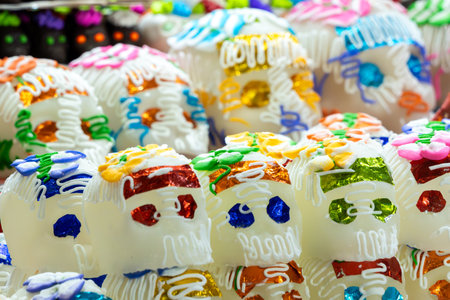 A variety of sugar skulls, each with its own unique design and color scheme. Mexican Day of the Dead tradition, offerings, food, colors, decorations, and papel picado, La Catrina.の写真素材