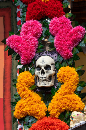 A skull is surrounded by flowers and leaves, with a heart and a pink flower on top. Mexican Day of the Dead tradition, offerings, food, colors, decorations, and papel picado, La Catrina.の写真素材