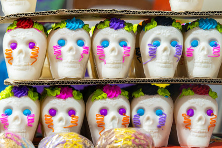 A stack of sugar skulls, each with a unique and colorful design, are arranged on a cardboard box. Mexican Day of the Dead tradition, offerings, food, colors, decorations, and papel picado, La Catrina.の写真素材