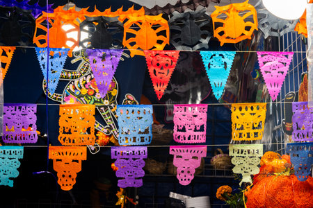 A colorful display of paper decorations with Mexican Day of the Dead themes. The decorations are hanging from a wire. Mexican Day of the Dead tradition, offerings, food, colors, decorations, and papel picado.の写真素材