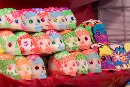 A table is covered with a variety of sugar skulls, each one uniquely decorated with frosting and bea. Mexican Day of the Dead tradition, offerings, food, colors, decorations, and papel picado, La Catrina.の写真素材