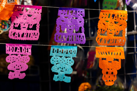 A row of colorful paper flags with the names of people on them. The flags are hanging on a wire. Mexican Day of the Dead tradition, offerings, food, colors, decorations, and papel picado, La Catrina.の写真素材