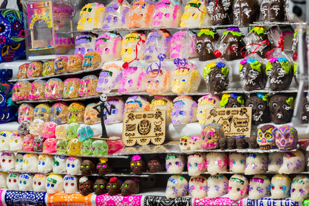 A display of sugar skulls with a sign that says "Juanita.". The skulls are in various colors. Mexican Day of the Dead tradition, offerings, food, colors, decorations, and papel picado, La Catrina.の写真素材