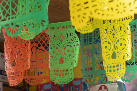 A colorful display of paper skulls hanging from the ceiling. The skulls are in various colors. Mexican Day of the Dead tradition, offerings, food, colors, decorations, and papel picado, La Catrina.の写真素材