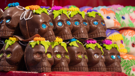 A row of chocolate skulls with green leaves on top. The skulls are decorated with colorful flowers. Mexican Day of the Dead tradition, offerings, food, colors, decorations, and papel picado, La Catrina.の写真素材