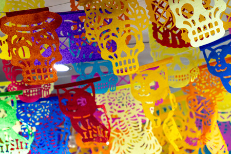 A colorful display of paper skulls hanging from the ceiling. The skulls are of various colors. Mexican Day of the Dead tradition, offerings, food, colors, decorations, and papel picado, La Catrina.の写真素材