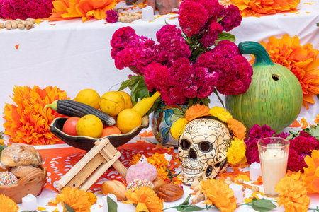 A table is covered with a variety of items, including a skull, flowers, fruits, and vegetables. Mexican Day of the Dead tradition, offerings, food, colors, decorations, and papel picado, La Catrina.の写真素材