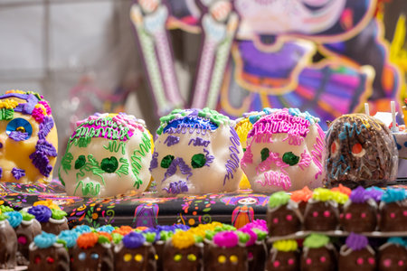 A table with three decorated skulls and a skeleton figure. The skulls are decorated with frosting. Mexican Day of the Dead tradition, offerings, food, colors, decorations, and papel picado, La Catrina.の写真素材
