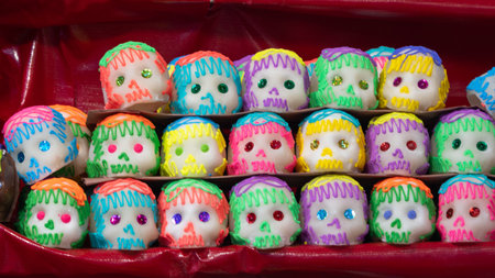 A row of colorful skulls with green, yellow, and purple paint. The skulls are decorated with glitter. Mexican Day of the Dead tradition, offerings, food, colors, decorations, and papel picado, La Catrina.の写真素材