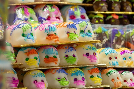 A variety of sugar skulls with different colors and designs are arranged on a shelf. Mexican Day of the Dead tradition, offerings, colors, decorations, and papel picado.の写真素材