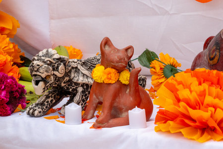 A cat figurine is sitting on a table with orange flowers. Mexican Day of the Dead tradition, offerings, food, colors, decorations, and papel picado, La Catrina.の写真素材