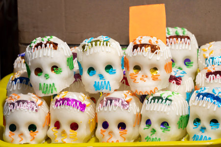 A tray of decorated skulls with colorful icing. The skulls are arranged in a row. Mexican Day of the Dead tradition, offerings, food, colors, decorations, and papel picado, La Catrina.の写真素材