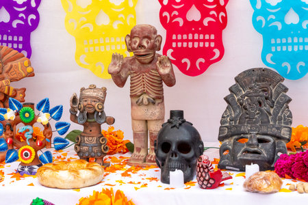 A table with a skull and other figures on it. The skull is surrounded by flowers. Mexican Day of the Dead tradition, offerings, food, colors, decorations, and papel picado, La Catrina.の写真素材