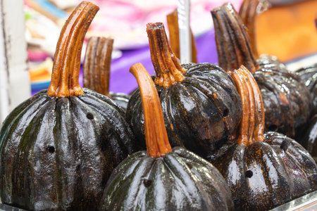A bunch of black pumpkins with brown stems. The pumpkins are sitting in a tray. The pumpkins are wet. Mexican Day of the Dead tradition, offerings, colors, decorations, and papel picado, La Catrina.の写真素材