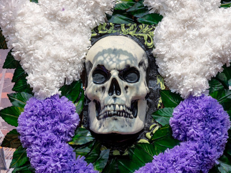 A skull is surrounded by purple flowers and white flowers. The skull is black and white. Mexican Day of the Dead tradition, offerings, food, colors, decorations, and papel picado, La Catrina.の写真素材