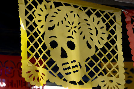 A yellow paper cutout of a skull with flowers on it. The skull is surrounded by a lattice of flowers. Mexican Day of the Dead tradition, offerings, food, colors, decorations, and papel picado, La Catrina.の写真素材