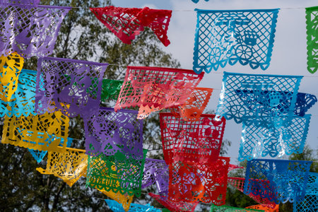 A colorful display of paper flags hanging from a tree. The flags are of different colors and sizes. Mexican Day of the Dead tradition, offerings, food, colors, decorations, and papel picado.の写真素材