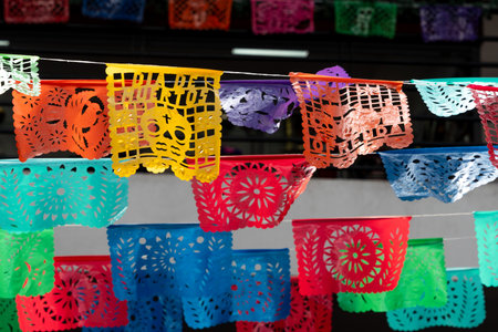 A colorful display of paper flags with a skull on one of them. The flags are hanging from a wire. Mexican Day of the Dead tradition, offerings, food, colors, decorations, and papel picado, La Catrina.の写真素材