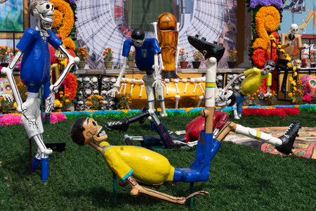 A group of skeletons are laying on the grass in a field. The skeletons are dressed in yellow. Mexican Day of the Dead tradition, offerings, food, colors, decorations, and papel picado, La Catrina.の写真素材
