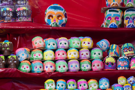 A table filled with a variety of decorated skulls and skeletons, arranged in a pyramid shape. Mexican Day of the Dead tradition, offerings, food, colors, decorations, and papel picado, La Catrina.の写真素材