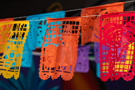 A colorful string of paper flags with a skull on them. The flags are hanging from a line. Mexican Day of the Dead tradition, offerings, food, colors, decorations, and papel picado, La Catrina.の写真素材