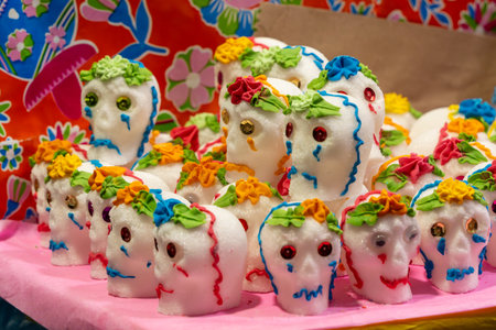 A table is covered with a pink background and decorated sugar skulls. The skulls are made of sugar. Mexican Day of the Dead tradition, offerings, food, colors, decorations, and papel picado, La Catrina.の写真素材