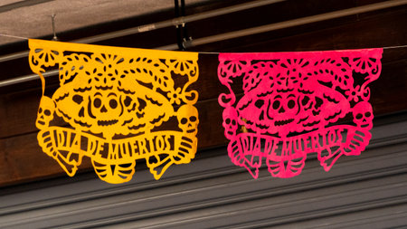 Two colorful paper lanterns with skulls and bones on them, one is yellow and the other is pink. Mexican Day of the Dead tradition, offerings, food, colors, decorations, and papel picado, La Catrina.の写真素材