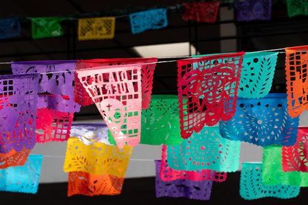 A colorful display of paper flags hanging from a wire. The flags are of different colors and sizes. Mexican Day of the Dead tradition, offerings, colors, decorations, and papel picado, La Catrina.の写真素材