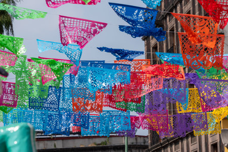 A colorful display of paper flags hangs from the ceiling. The flags are in various colors and shapes. Mexican Day of the Dead tradition, offerings, food, colors, decorations, and papel picado, La Catrina.の写真素材