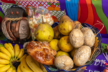 A bowl of fruit and bread on a table. The fruit includes bananas, oranges, and coconuts. Mexican Day of the Dead tradition, offerings, food, colors, decorations, and papel picado.の写真素材