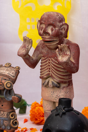 A skeleton statue is sitting on a table with other statues and a skull. The statue is wearing a mask. Mexican Day of the Dead tradition, offerings, food, colors, decorations, and papel picado, La Catrina.の写真素材