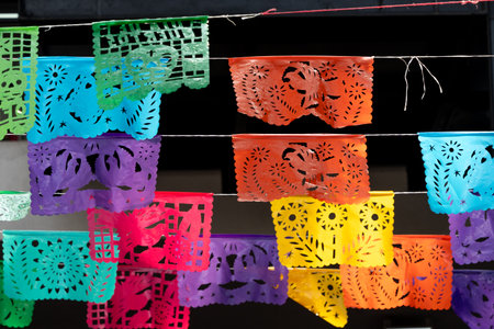 A colorful array of paper decorations hang from a string. The decorations are of various colors and sizes. Mexican Day of the Dead tradition, offerings, colors, decorations, and papel picado.の写真素材