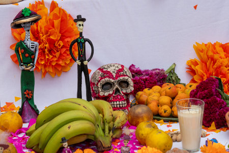 A table with a skull, two skeletons, and fruit. The skull is surrounded by bananas and oranges. Mexican Day of the Dead tradition, offerings, food, colors, decorations, and papel picado, La Catrina.の写真素材