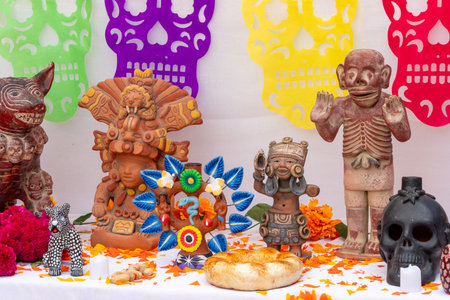 A table with a variety of Mexican themed items including skulls, skeletons, and figurines. Mexican Day of the Dead tradition, offerings, food, colors, decorations, and papel picado, La Catrina.の写真素材