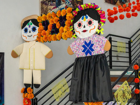 A man and woman are dressed in traditional Mexican clothing and are standing on a staircase. Mexican Day of the Dead tradition, offerings, food, colors, decorations, and papel picado.の写真素材