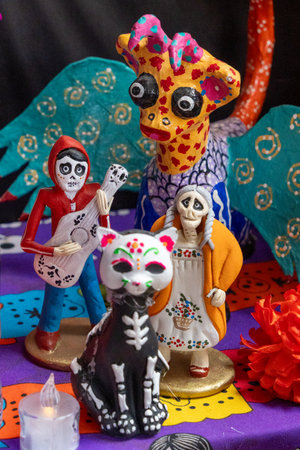 A table is decorated with three figurines, one of which is a skeleton. Mexican Day of the Dead tradition, offerings, food, colors, decorations, and papel picado, La Catrina.の写真素材