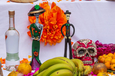 A table with a skeleton, two skeletons, a bottle of liquor, and a bunch of bananas. Mexican Day of the Dead tradition, offerings, food, colors, decorations, and papel picado, La Catrina.の写真素材