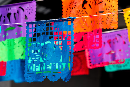 A colorful banner with the word written on it. The banner is hanging from a string. Mexican Day of the Dead tradition, offerings, food, colors, decorations, and papel picado, La Catrina.の写真素材