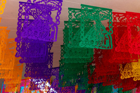 A colorful string of paper lanterns hang from the ceiling. The lanterns are in various colors. Mexican Day of the Dead tradition, offerings, food, colors, decorations, and papel picado, La Catrina.の写真素材