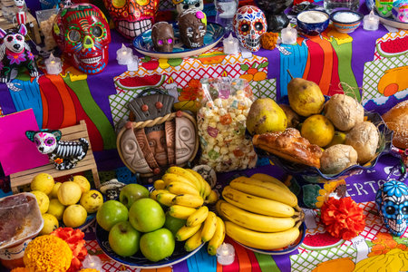 A table is covered with a colorful tablecloth and a variety of fruits and vegetables. Mexican Day of the Dead tradition, offerings, food, colors, decorations, and papel picado, La Catrina.の写真素材