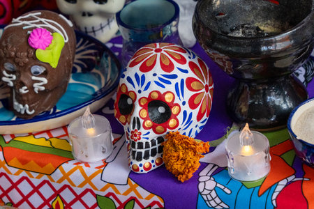 A table with a skull decoration and candles on it. The skull decoration is decorated with flowers. Mexican Day of the Dead tradition, offerings, food, colors, decorations, and papel picado, La Catrina.の写真素材