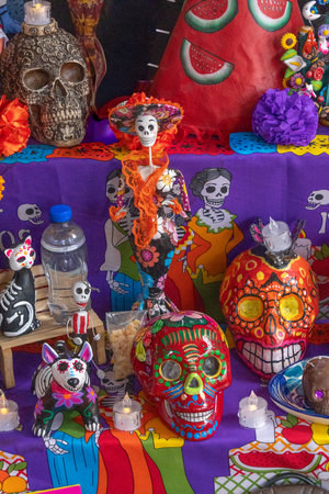 A table covered in various decorations including skulls, skeletons, and a woman in a sombr. Mexican Day of the Dead tradition, offerings, food, colors, decorations, and papel picado, La Catrina.の写真素材