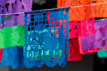 A blue and red paper with the word "ofrenda" written on it. The paper is hanging from a string. Mexican Day of the Dead tradition, offerings, food, colors, decorations, and papel picado, La Catrina.の写真素材