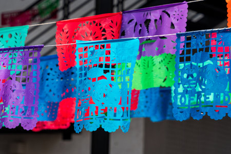 A colorful display of paper flags hanging from a line. The flags are in various colors and patterns. Mexican Day of the Dead tradition, offerings, food, colors, decorations, and papel picado, La Catrina.の写真素材
