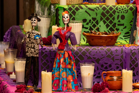 A table with two skeletons and a couple of cups. The table is decorated with a purple. Mexican Day of the Dead tradition, offerings, food, colors, decorations, and papel picado, La Catrina.の写真素材