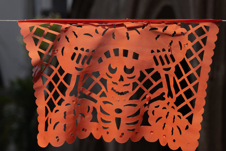 A skeleton is hanging from a red and white paper lantern. The skeleton is wearing a sombrero. Mexican Day of the Dead tradition, offerings, food, colors, decorations, and papel picado, La Catrina.の写真素材