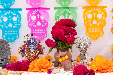 A table with a vase of red flowers and a skull decoration.Mexican Day of the Dead tradition, offerings, food, colors, decorations, and papel picado, La Catrina.の写真素材