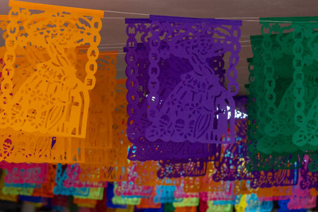 A colorful string of paper lanterns hang from the ceiling. The lanterns are in various colors. Mexican Day of the Dead tradition, offerings, food, colors, decorations, and papel picado, La Catrina.の写真素材