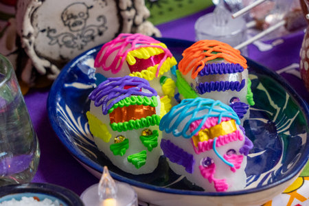 A bowl of colorful sugar skulls sits on a table. The skulls are decorated with frosting. Mexican Day of the Dead tradition, offerings, food, colors, decorations, and papel picado, La Catrina.の写真素材