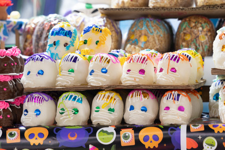 A display of decorated sugar skulls on a table. The skulls are colorful and have a festive. Mexican Day of the Dead tradition, offerings, food, colors, decorations, and papel picado, La Catrina.の写真素材